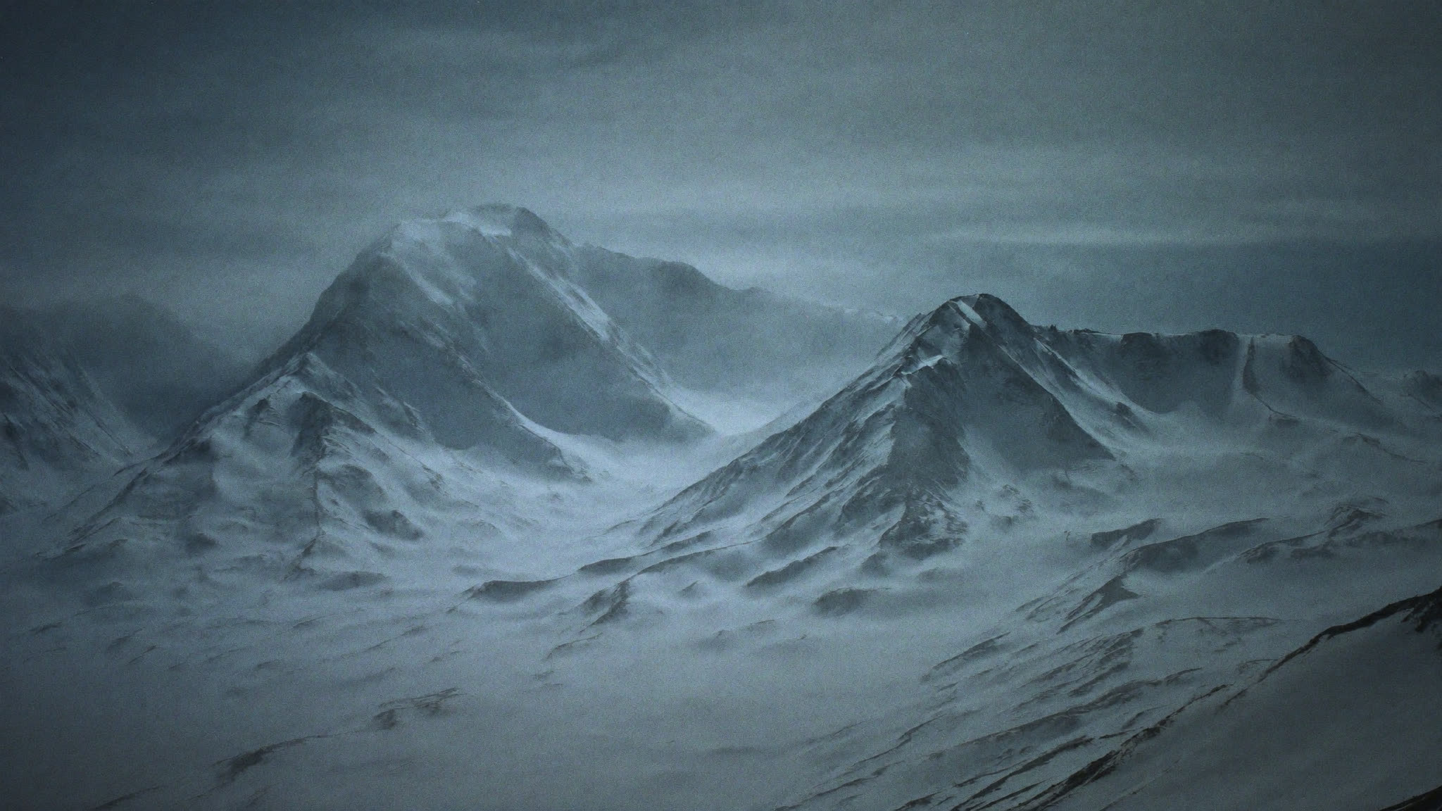 Snow-covered mountain range under a cold overcast sky